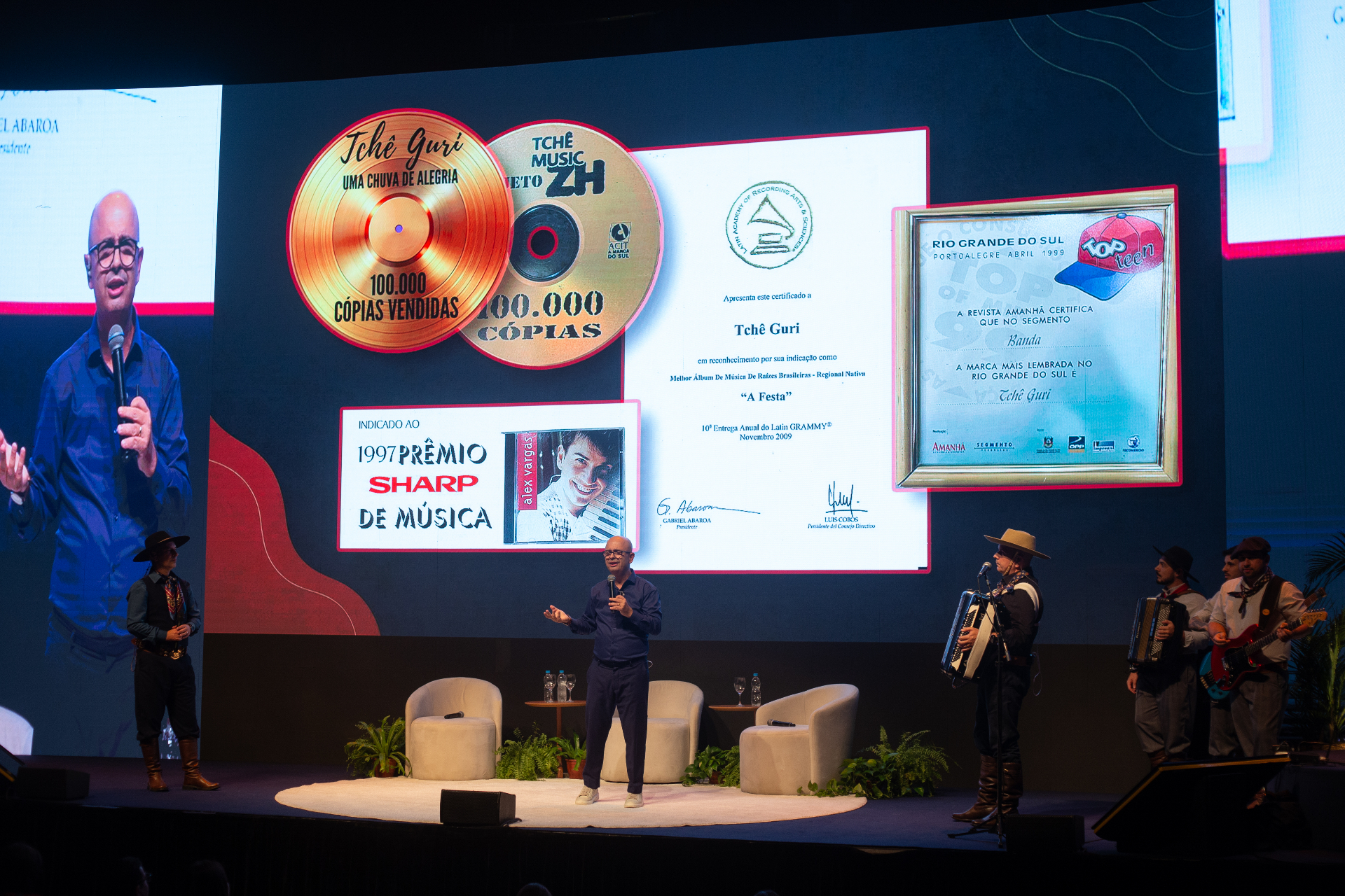 Fabinho Vargas no palco com troféus e prêmios do Tchê Guri ao fundo